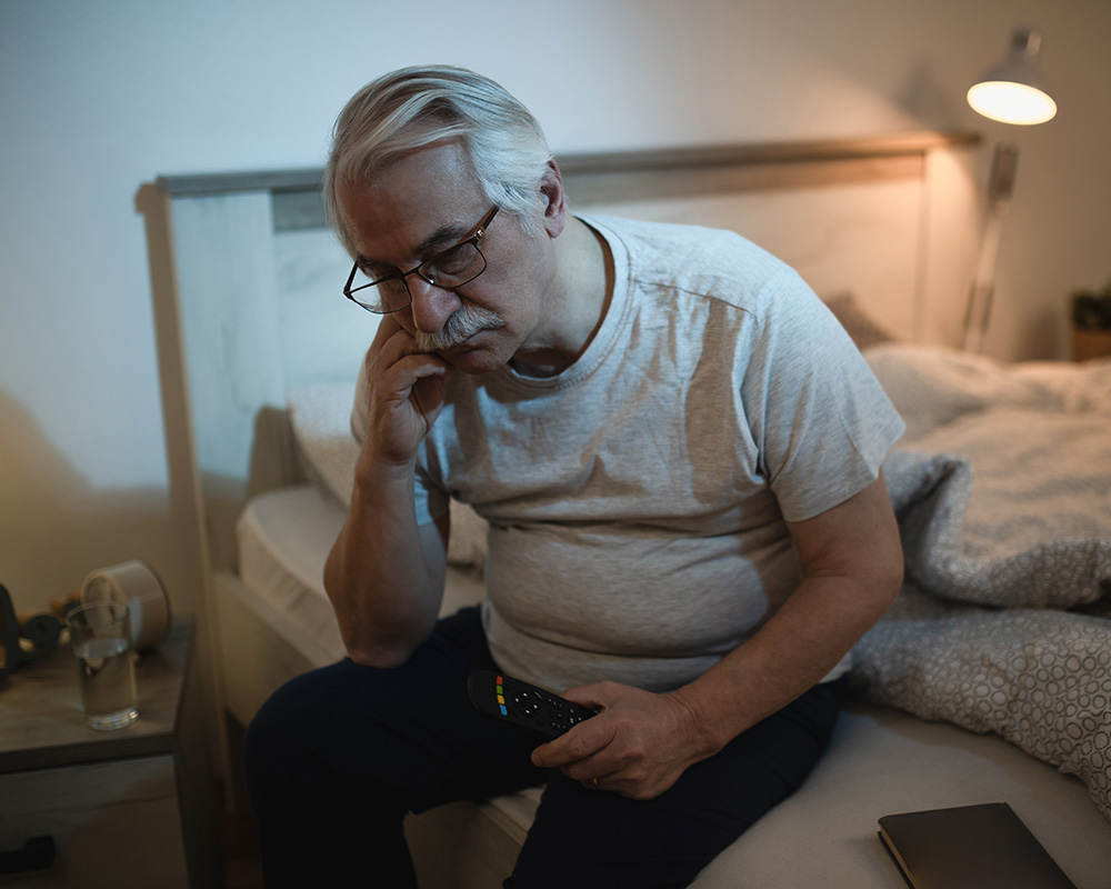 A sleepless man sitting up in his bed contemplating