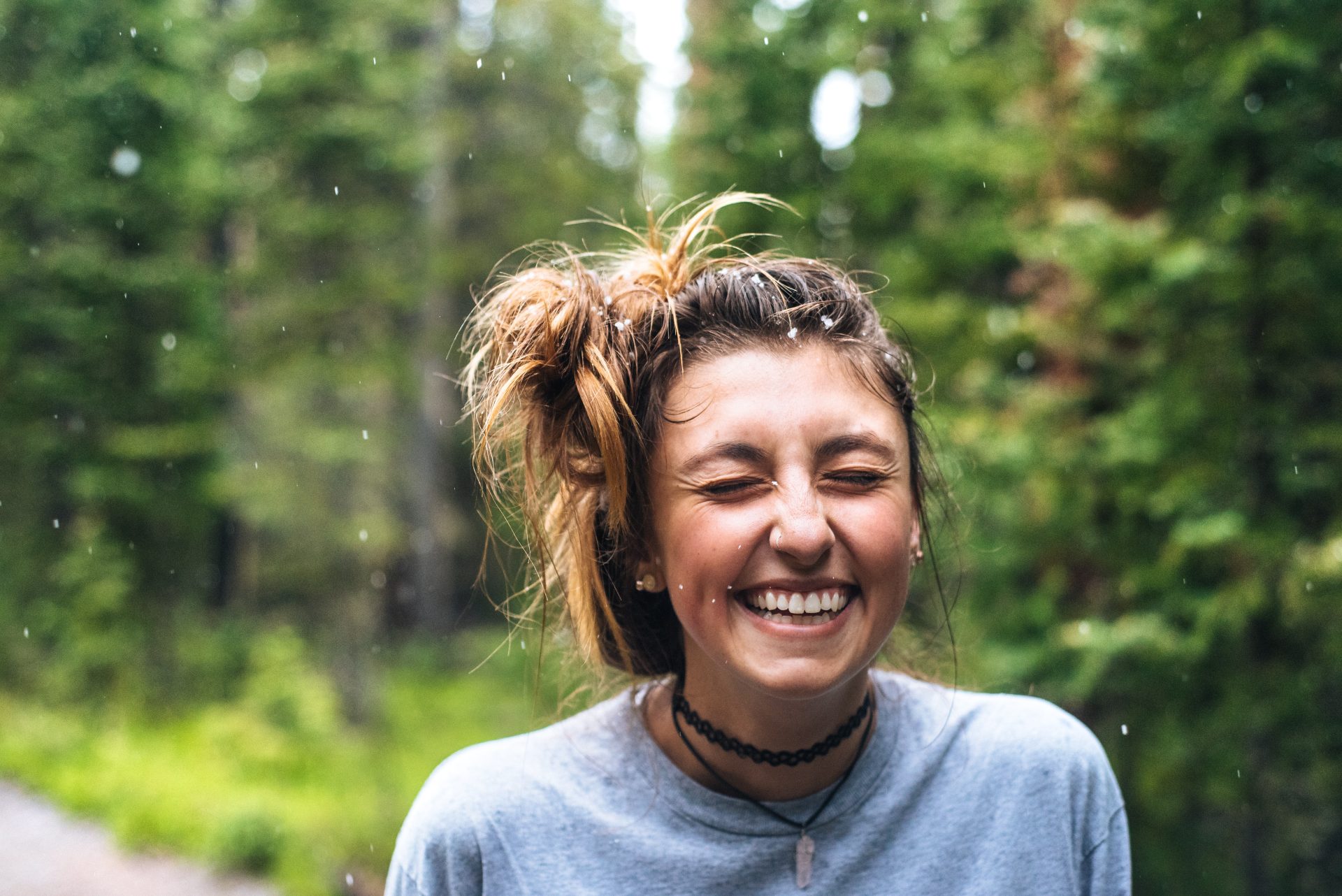 teenager with brown hair smiling and laughing on road in front of a wooded area